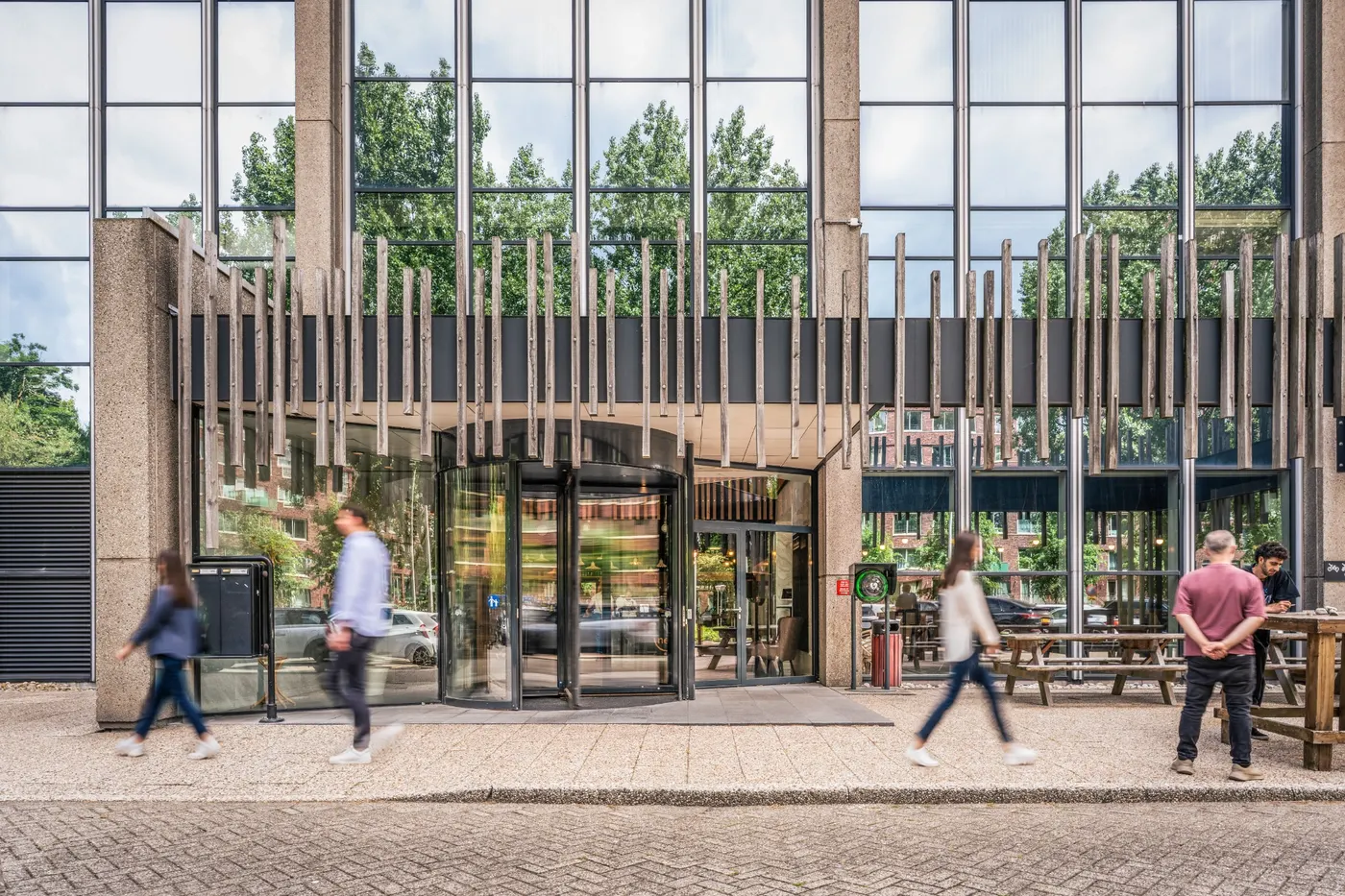 Entree van het kantoorgebouw van Nest Werkplekken in Amstelveen met glazen gevel en voorbijlopende bezoekers.
