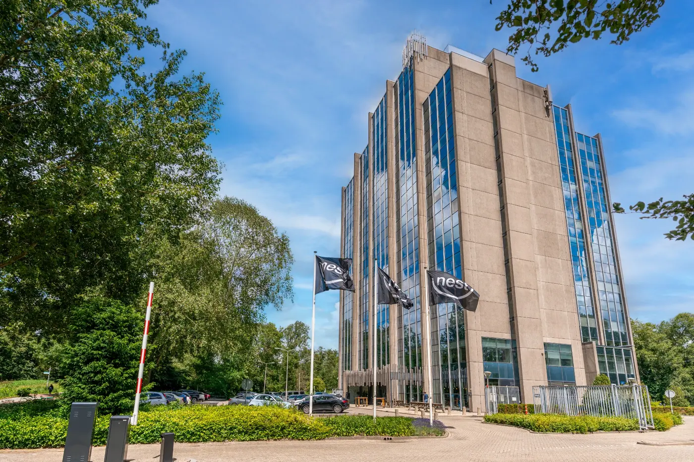 Kantoorgebouw van Nest Werkplekken in Amstelveen met Nest-vlaggen bij de entree en groen rondom het pand