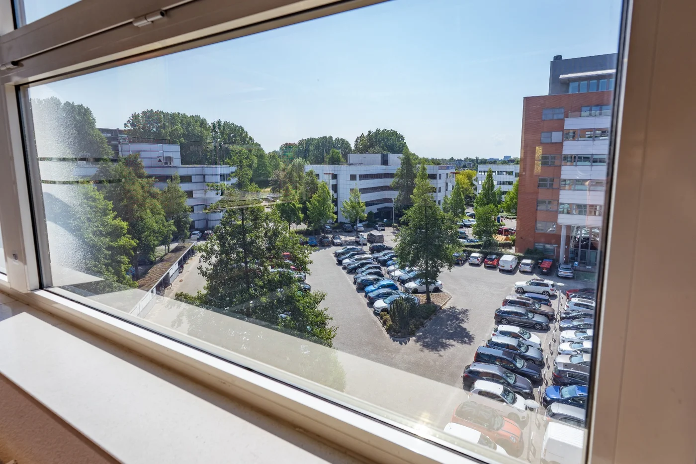 Uitzicht vanuit een kantoor van Nest Werkplekken in Amsterdam Zuidoost op de groene omgeving en parkeerplaatsen
